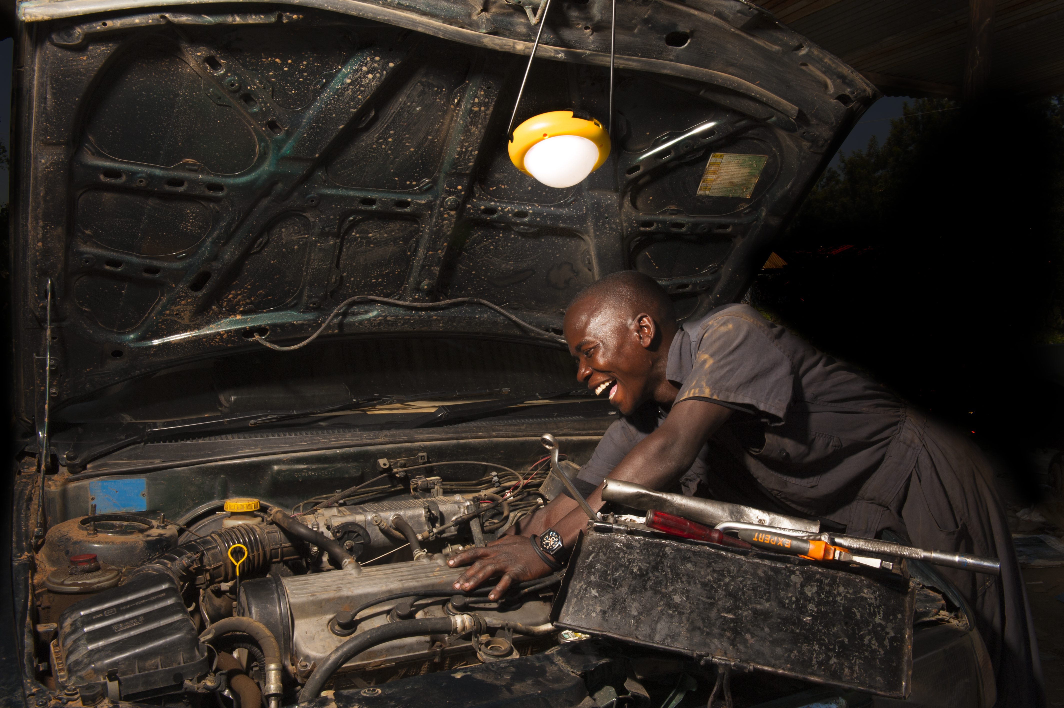 African man mechanic working on car engine by solar light