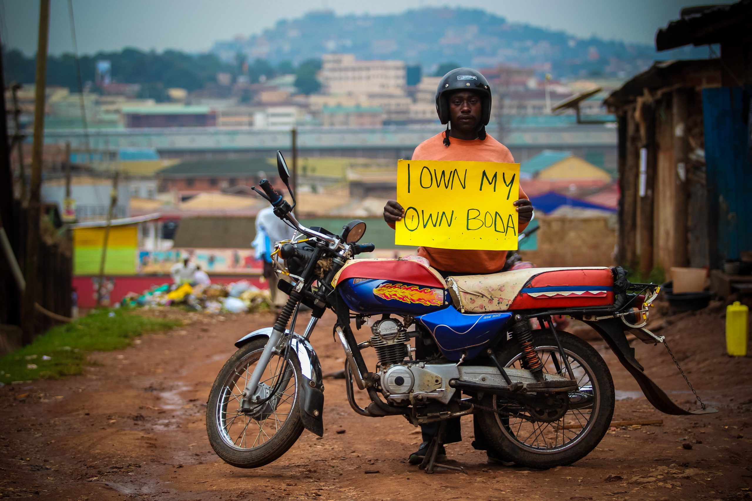 Image of man with motorbike holding a sign saying 'I own my boda boda'