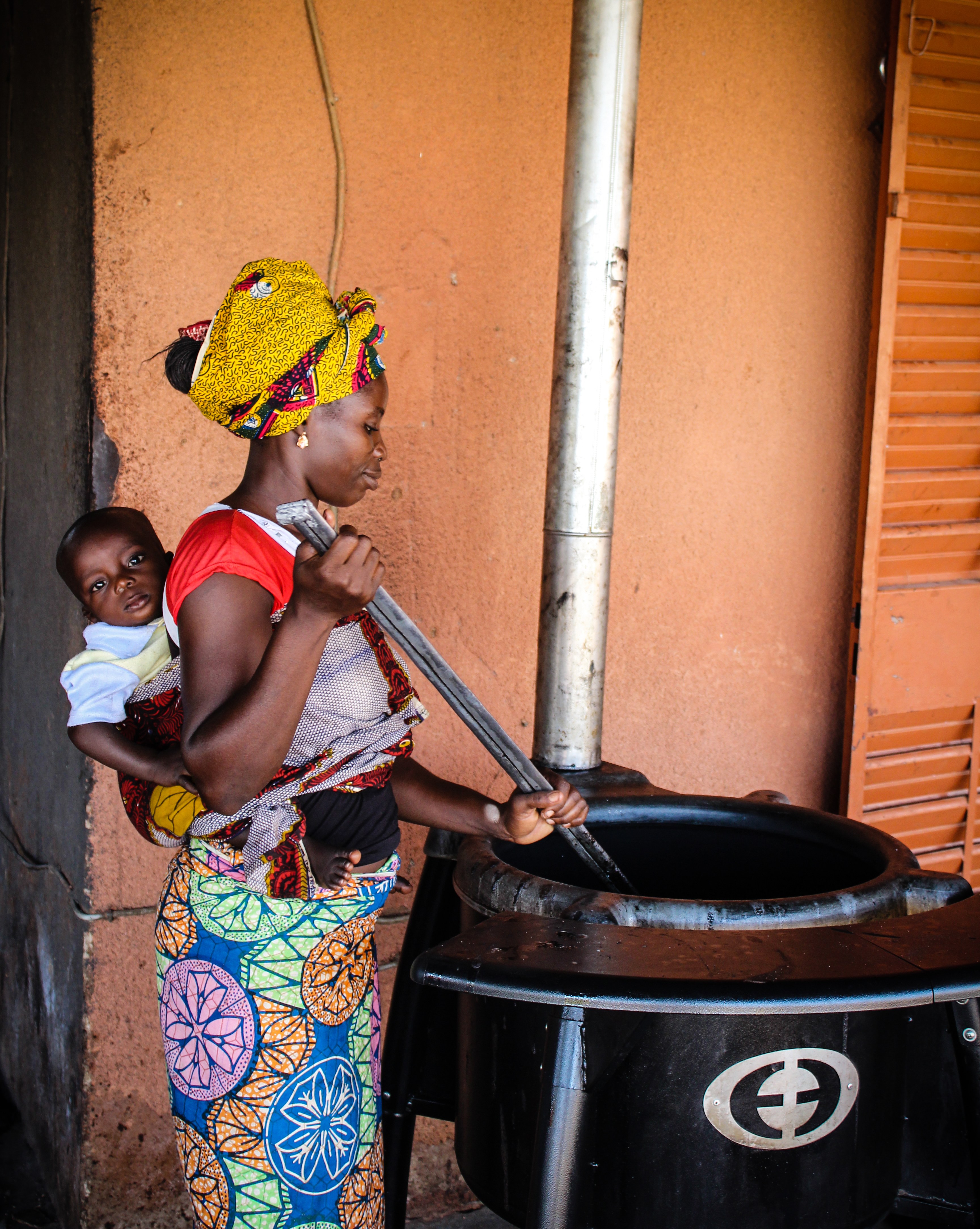 African lady baby on back in sling cooking on large Envirofit stove