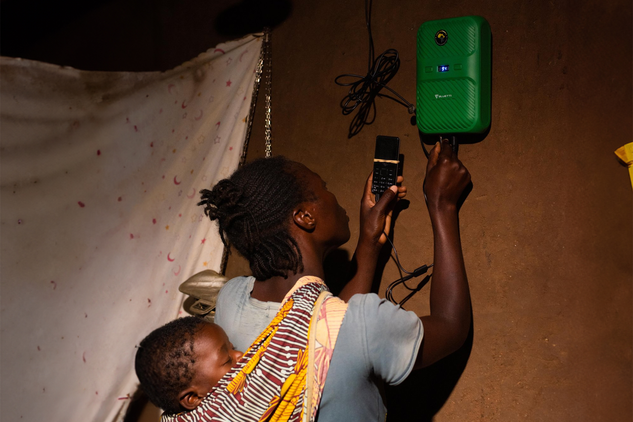 Woman with baby plugging in her mobile phone to a power bank on the wall