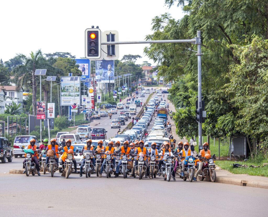 A line of motorbike taxi drivers wait at traffic lights at a city junction