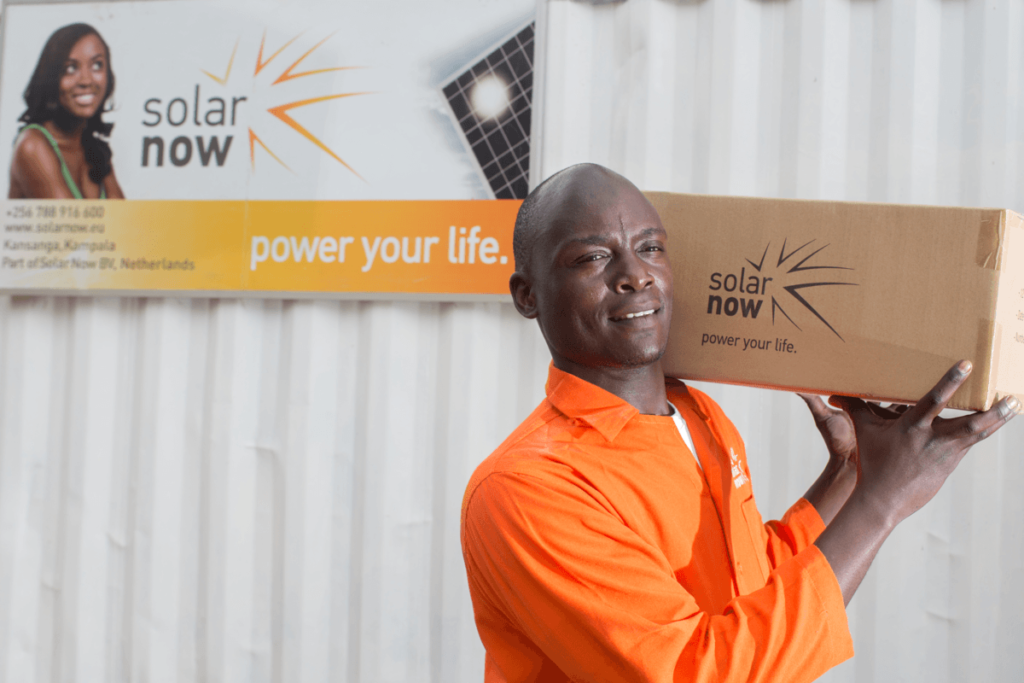 Man carrying bx with Solar Now branding and poster in background