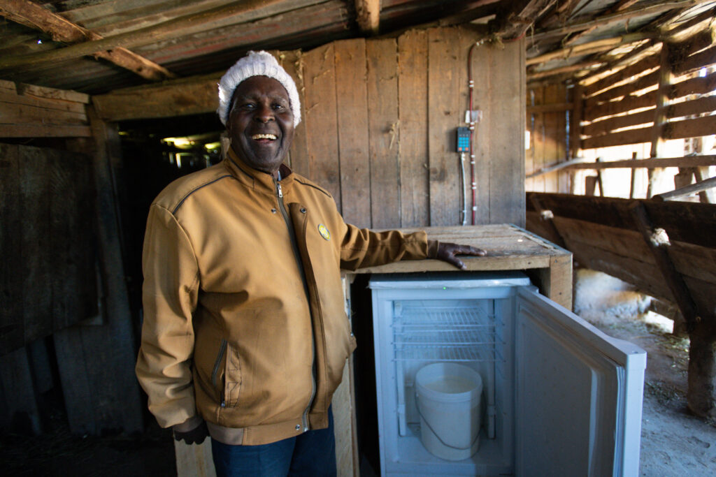 Kenyan Dairy Farmer smiling with SureChill Fridge with milk in it